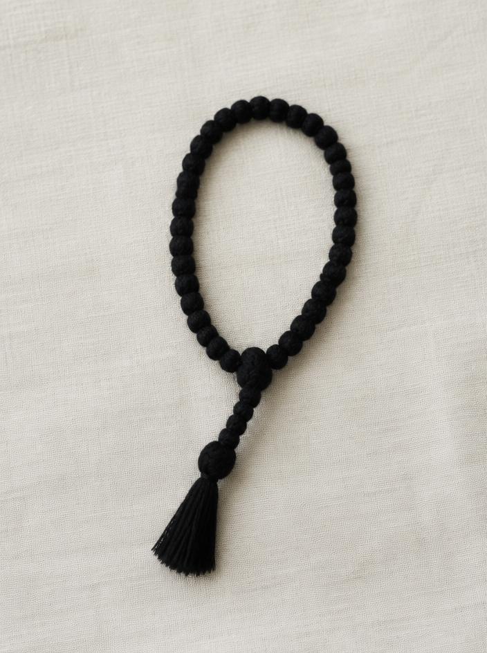 Black knotted wool prayer rope with a tassel on cream linen
