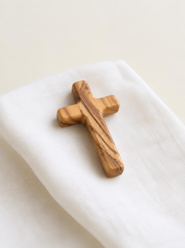 Small olive wood hand cross resting on white linen